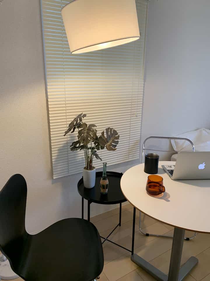 ホワイトとブラックのトーンの6畳のワンルーム、サイドテーブルと植物が配置されたモダンなホームオフィス風インテリア