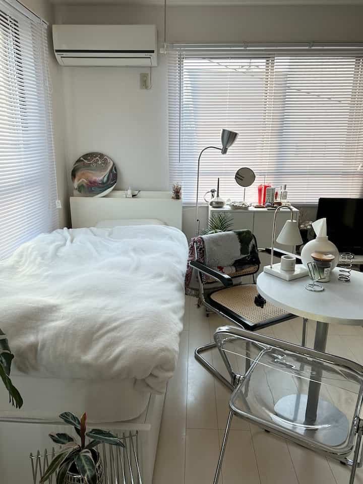 ホワイトトーンの寝室、整えられたベッドと透明な椅子が配置された清潔で明るい雰囲気のインテリア