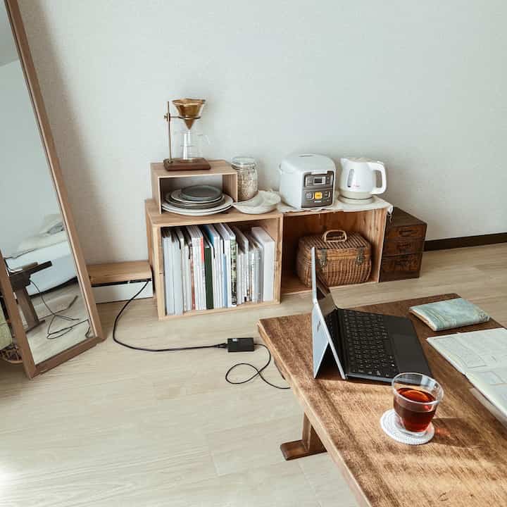 ナチュラルな色調の狭い部屋に、ローテーブルや本棚、コーヒー器具が配置されたシンプルな在宅勤務スペース