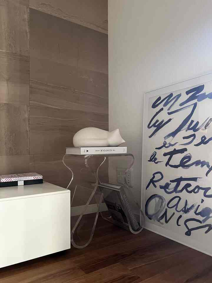 A corner of the living room in white and wood tones featuring a transparent stool and cat-shaped decor with a minimalistic vibe