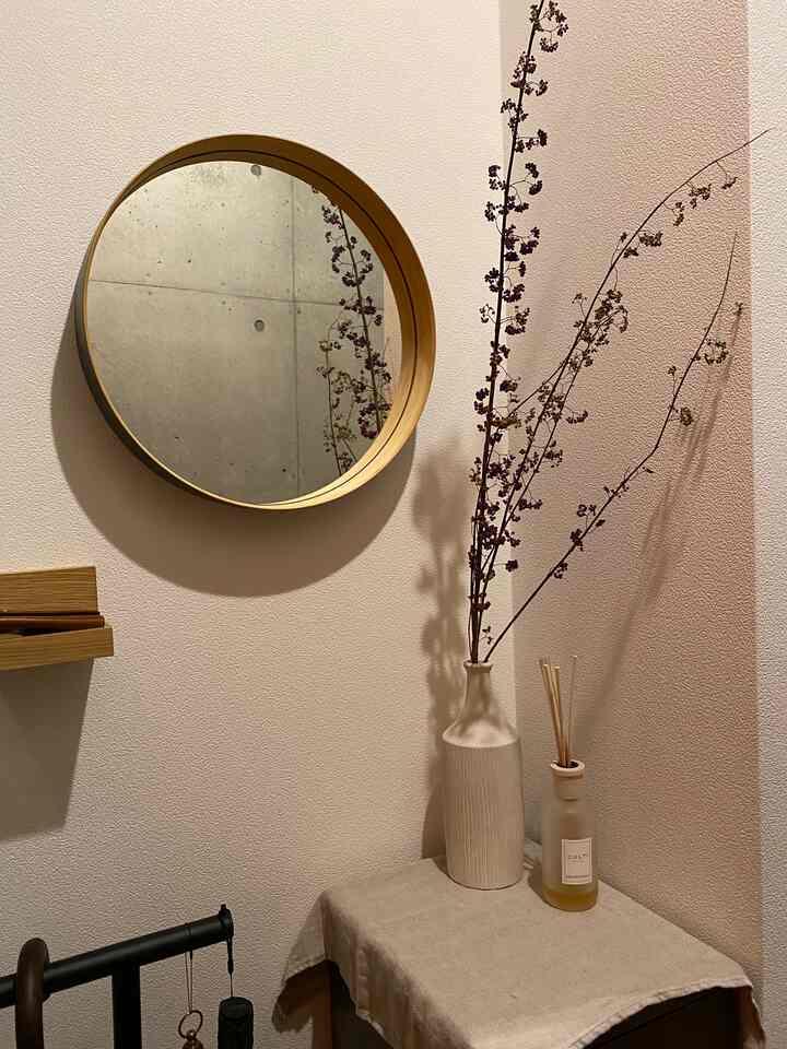 Beige-toned walls with a wood-toned round mirror and diffuser in a natural-feeling small living space