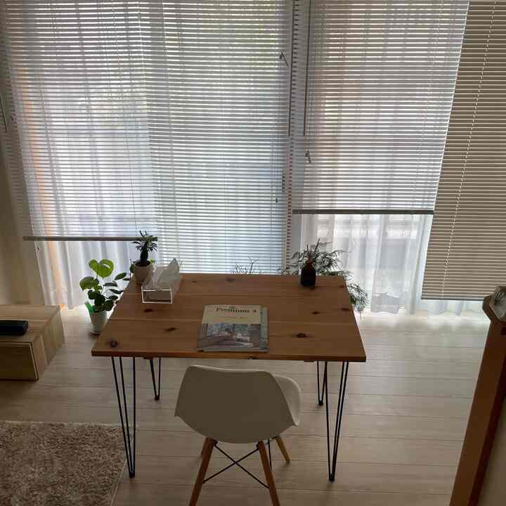 明るい木目調の床とカーテンがあるワンルーム、木製テーブルと白い椅子が配置された雰囲気のあるインテリア