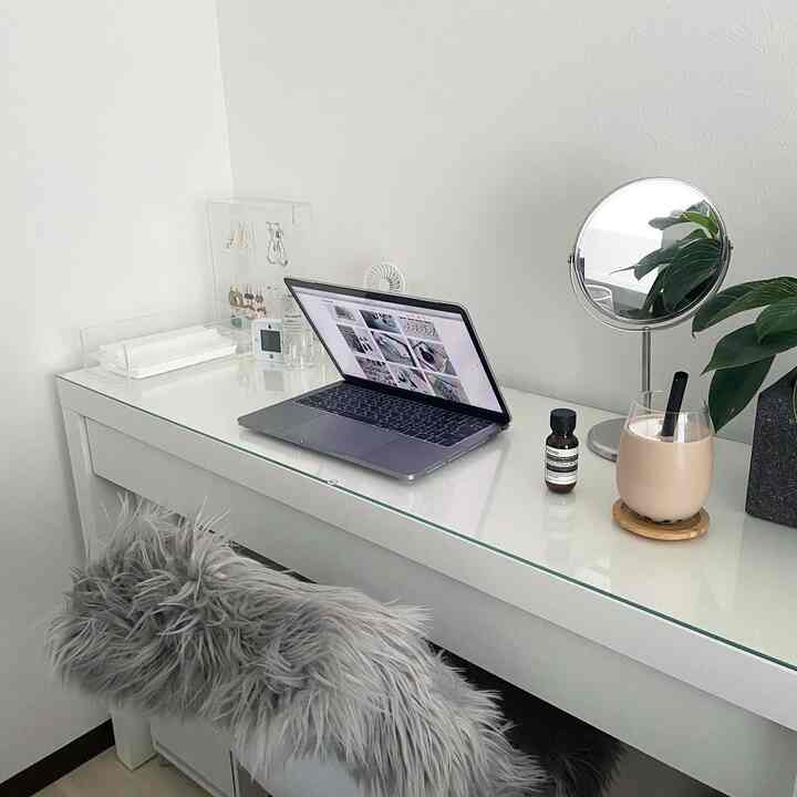 White-toned walk-in closet workspace with a clean desk featuring a laptop, vanity mirror, and clear acrylic jewelry organizer