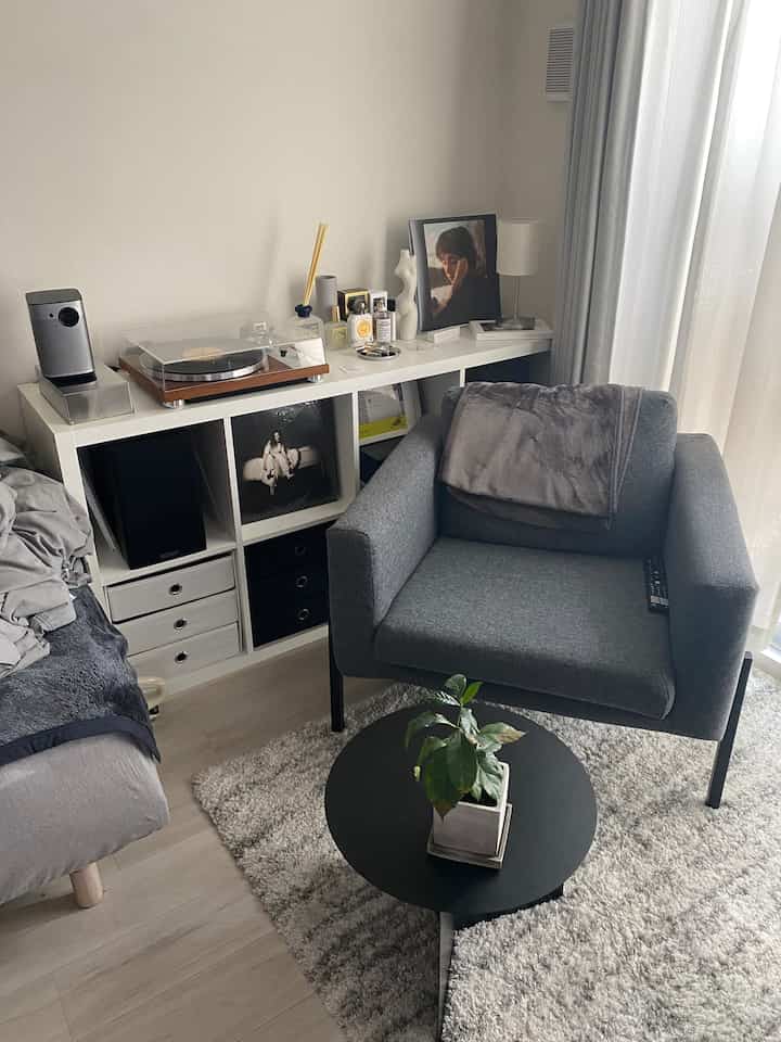 グレーのモノトーン調リビング、中央にアームチェアとラグを配置し、手前には黒い円形のサイドテーブルがある落ち着いた空間