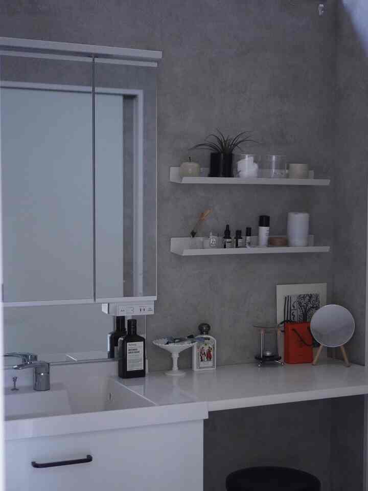 グレーの壁と白い洗面台、すっきりした棚が配置されたミニマルなバスルームインテリア