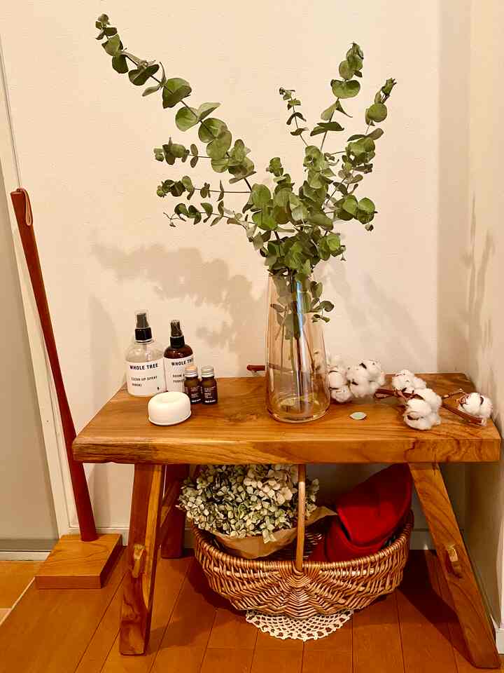 暖かいブラウンの木目調が印象的な玄関、チェリー材のベンチにディフューザーとスプレーが置かれ、下にはバスケットの収納スペースがあるナチュラルなインテリア