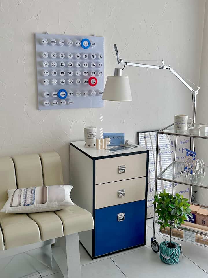 ホワイトの壁とネイビー・ベージュのアクセントが調和するダイニング、洗練された3段チェストと金属製キッチンワゴンが置かれたミニマルで自然な雰囲気のインテリア