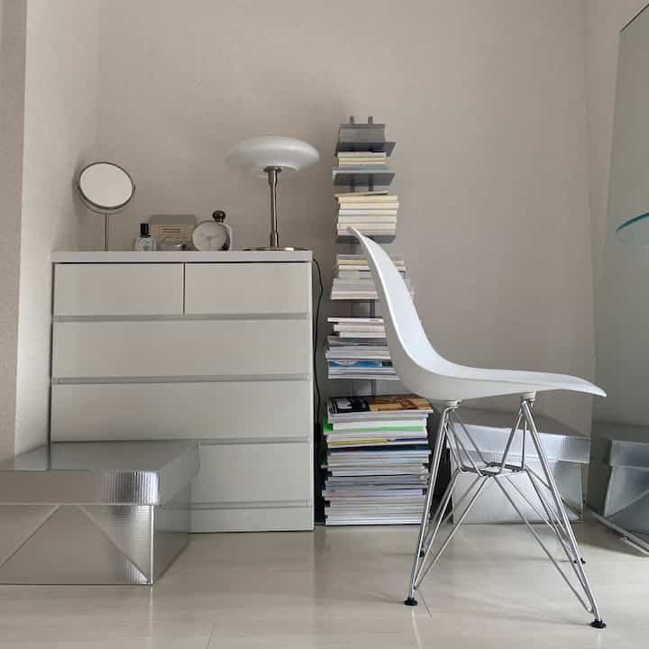 ホワイトとシルバーのトーンでまとめられたミニマルなリビング、ドレッサー、ダイニングチェア、本棚が配置された印象的な空間