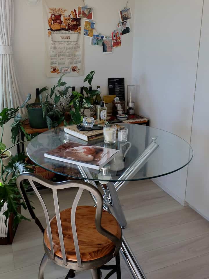 Natural modern dining room with transparent glass round table and wooden chair, featuring various plants and candles creating a cozy atmosphere