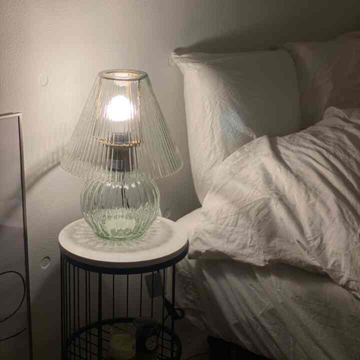 白を基調とした寝室、ガラスのテーブルランプときれいな寝具が配置された落ち着いた空間