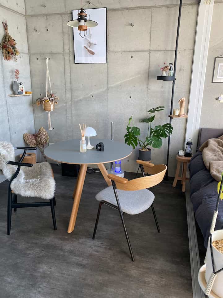 A natural modern living room with gray concrete walls and brown wood furniture, featuring a round table and armchairs in a cozy setting