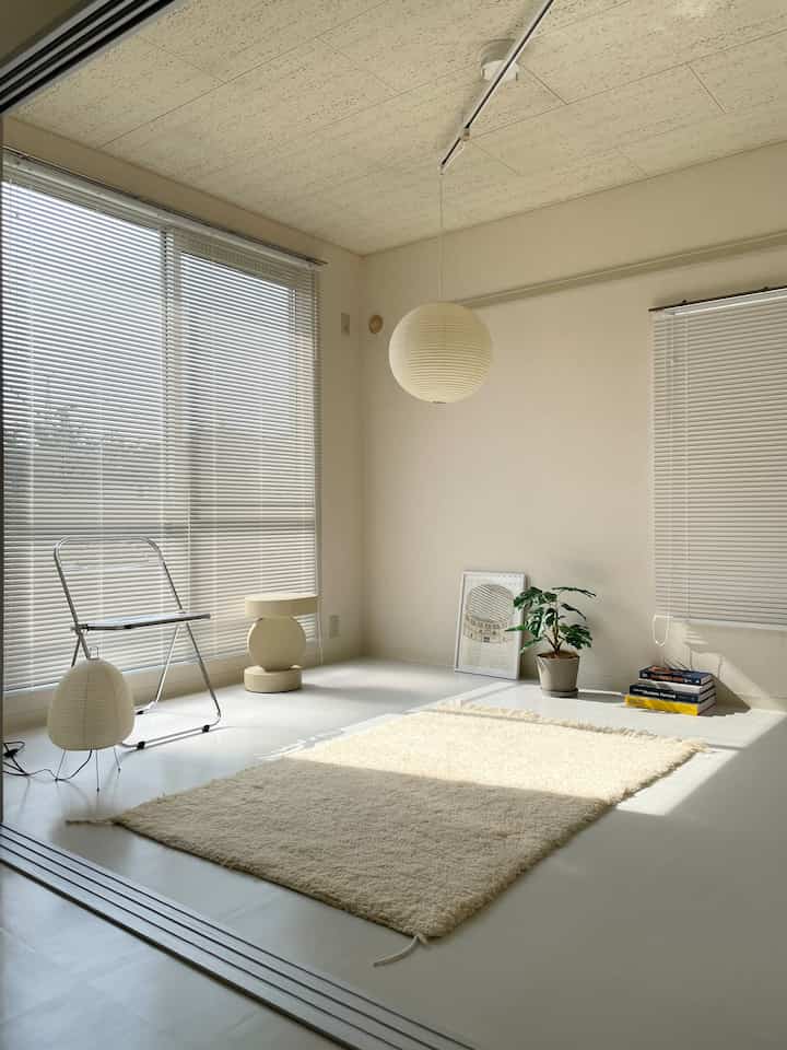 ホワイトとナチュラルな色調のリビング、ラグとスツールが配置されたシンプルでミニマルな雰囲気のインテリア