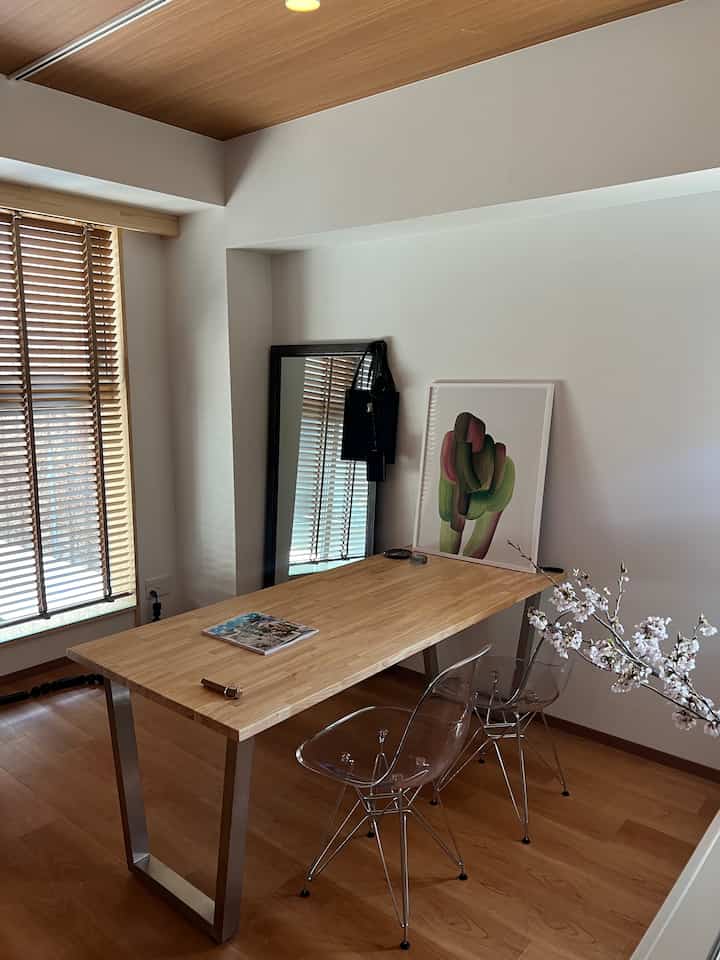 温かみのある木目調と自然光が特徴のナチュラルスタイルのホームオフィス、シンプルなデスクと透明なチェアが配置されたミニマルな空間