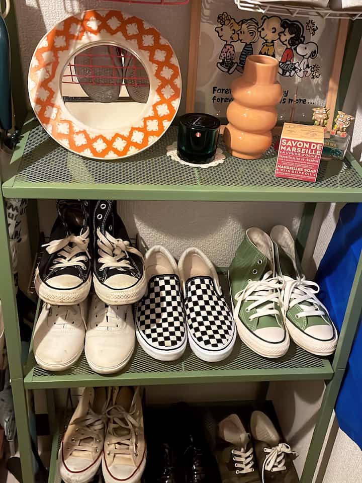 Light green steel rack with various shoes in a compact entrance area, decorated with objets and candles on upper shelf for practical storage