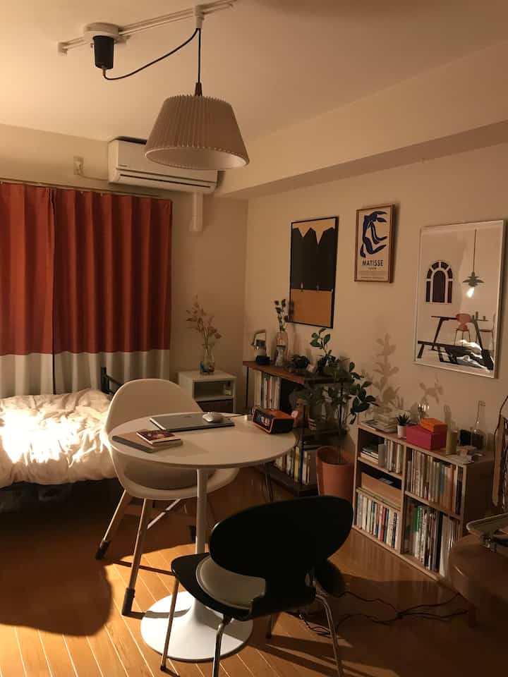 暖かいナチュラルカラーの寝室、丸いダイニングテーブルと本棚が配置され、居心地の良い雰囲気のあるインテリア