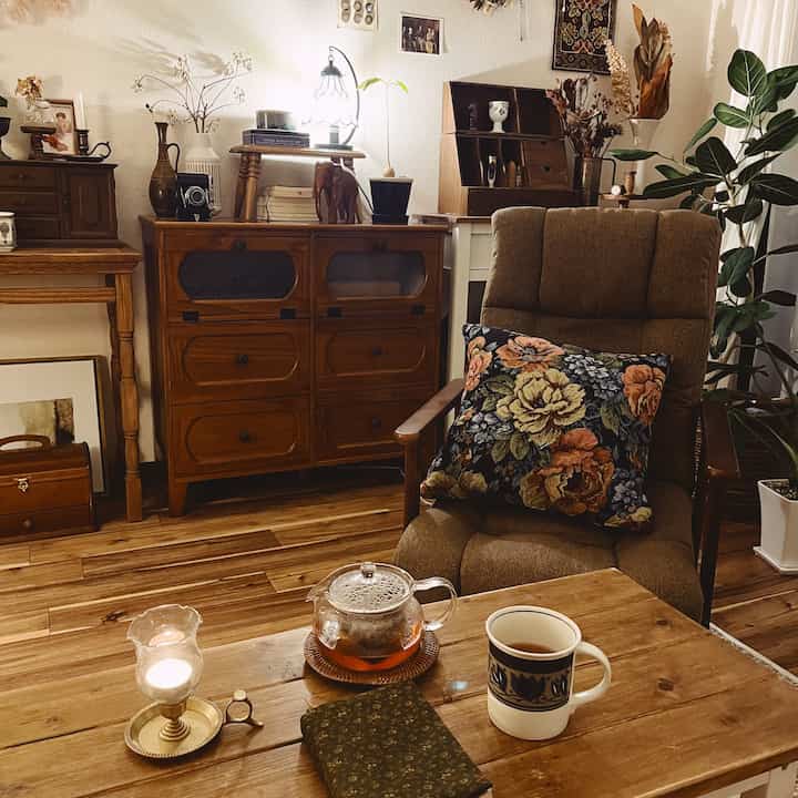 ナチュラルな色調のリビング、木製テーブルとアームチェア、レトロなチェストが配置された雰囲気のある空間