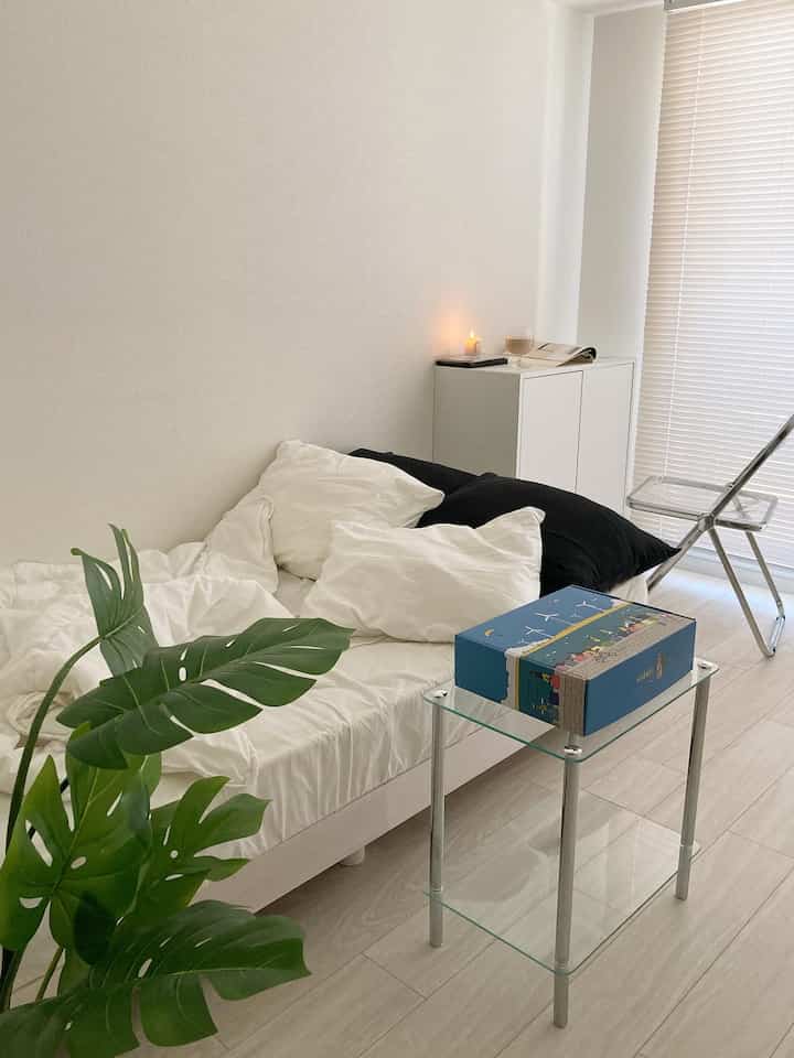 白とナチュラルカラーの寝室、モンステラの植物とガラスのサイドテーブルが配置された印象的な空間