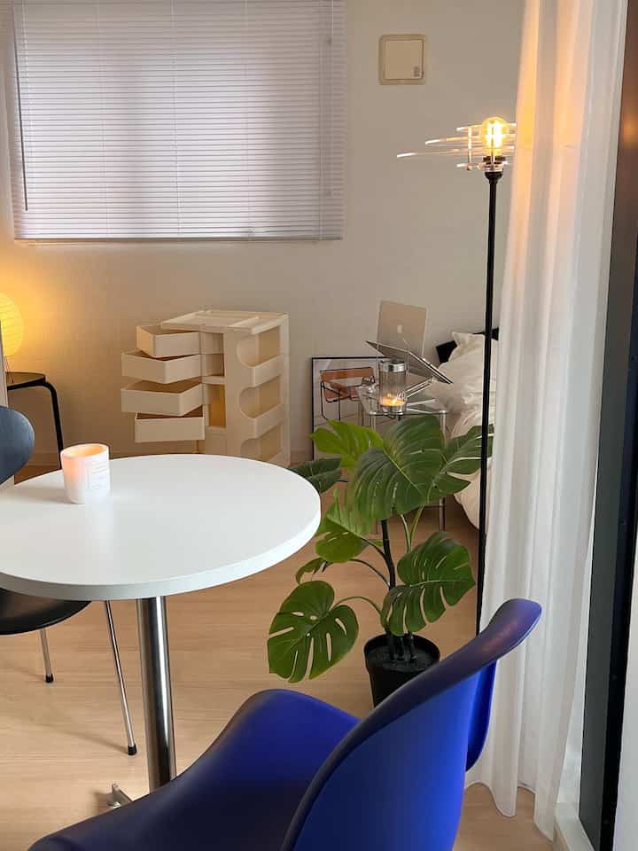 ホワイトとブルーのトーンでまとめられたコンパクトなモダンなワンルーム、円形のテーブルとモンステラの植物が配置された雰囲気のあるインテリア