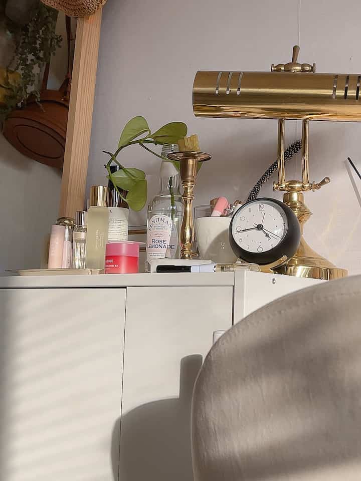 白とゴールドのキャビネットの上にテーブルランプ、時計、植物が配置された雰囲気のある収納スペース