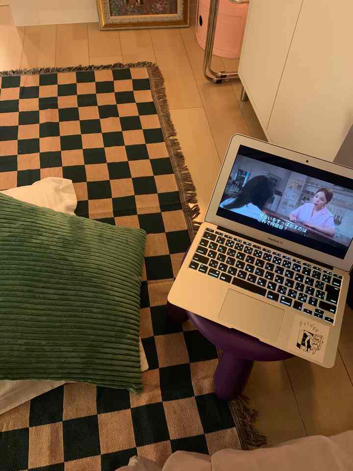 Beige and black checkered rug with a green cushion and purple stool in a compact home office setting