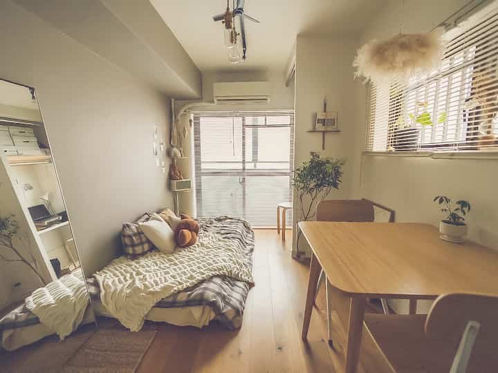 温かみのあるナチュラルな木目調の小さなワンルームダイニング、ベッドやダイニングテーブル、植物が配された印象的な空間