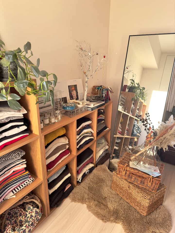 温かみのあるナチュラルカラーのクローゼット空間で、木製棚と全身鏡が配置され、落ち着いた整理された雰囲気のインテリア