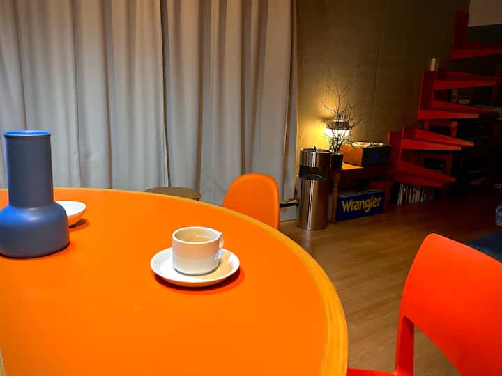 Bright orange semi-circular dining table with chairs in a living room, light brown wood flooring, and simple lighting creating a cozy atmosphere