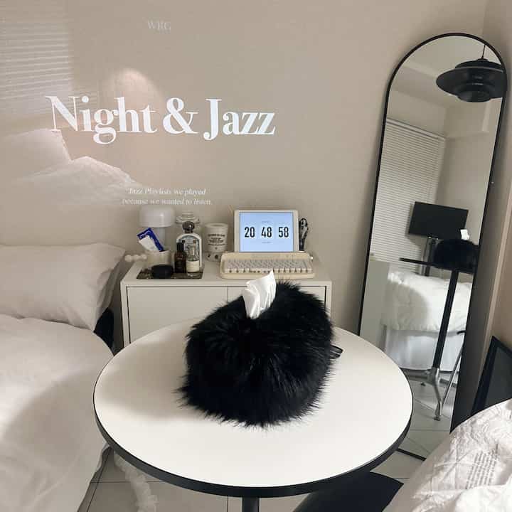 White and black toned studio bedroom featuring a round table, bed, full-length mirror, and nightstand with a modern atmosphere