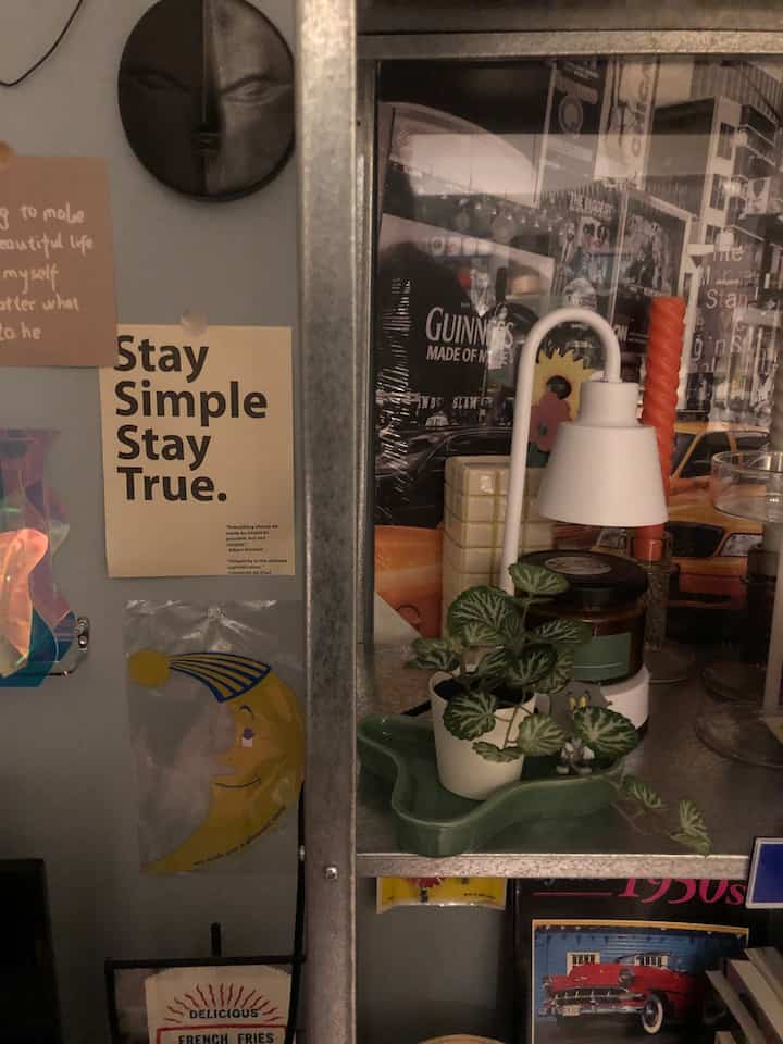 落ち着いたトーンのリビング壁、シンプルなポスターと金属製シェルフに植物とキャンドルが配置された雰囲気のあるインテリア