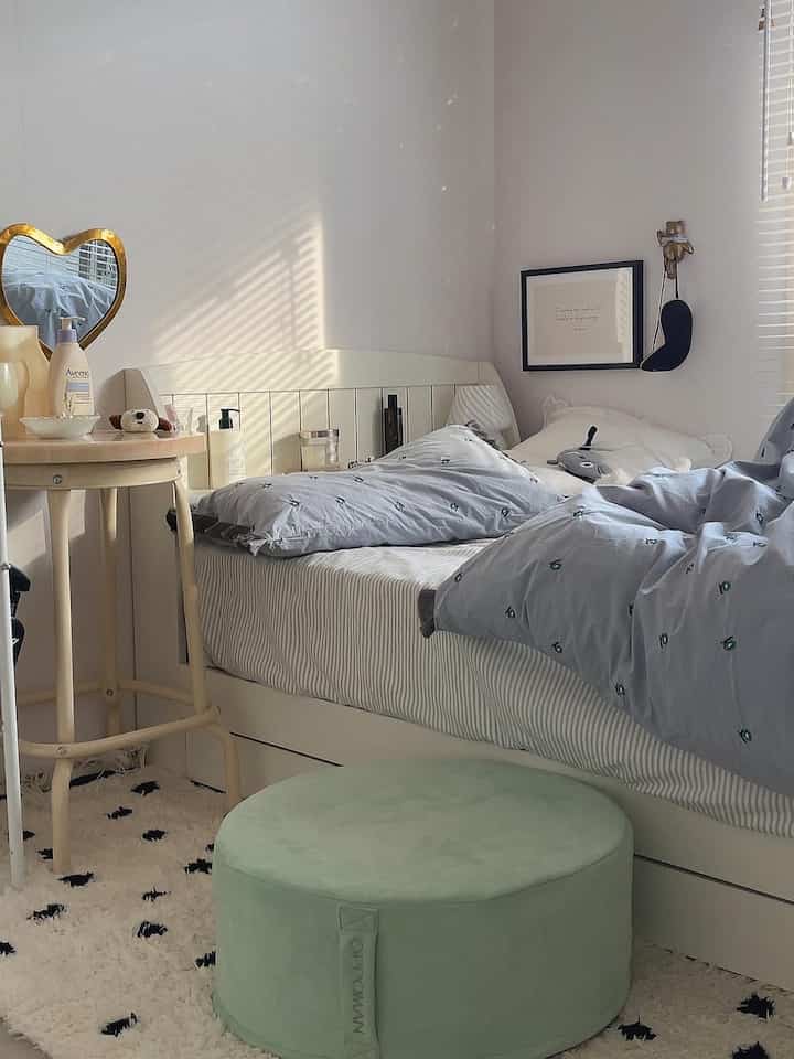 Bright white and light gray toned bedroom featuring soft cushions and a round wooden stool creating a cozy atmosphere