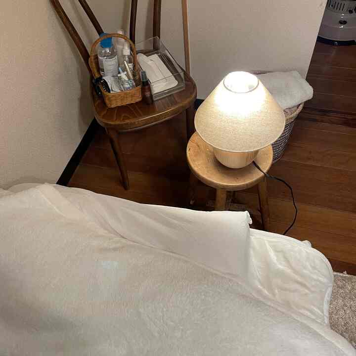 木目調とホワイトが調和する居心地の良い寝室、木製の椅子とスツールに置かれた照明と収納小物がある雰囲気のあるインテリア