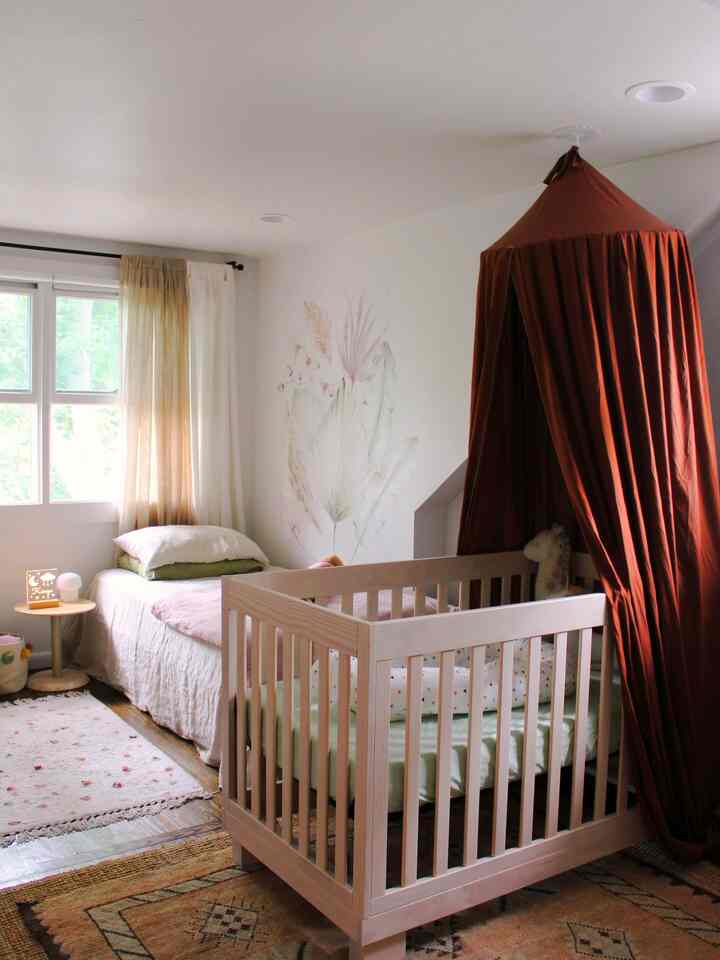 Bright white and brown wood-toned nursery featuring a crib, single bed, curtains, and rugs with cozy natural modern atmosphere
