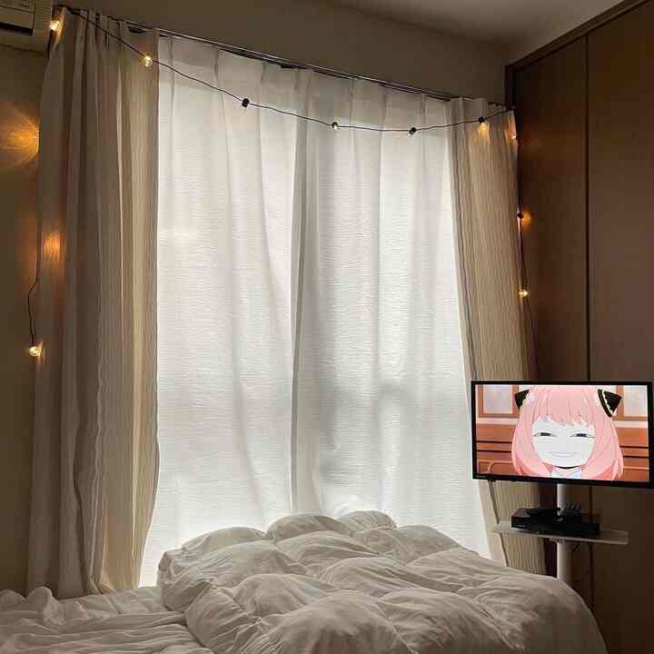 白いカーテンとダークブラウンの壁がある一人用寝室、暖かい白い寝具と間接照明のストリングライトで居心地の良い空間