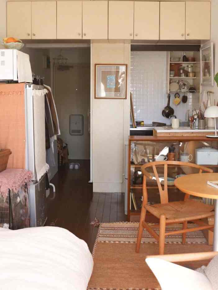 白と茶色のトーンが特徴のワンルームリビング兼キッチン、ナチュラルな木製家具とラグが温かみのある雰囲気を醸し出す空間