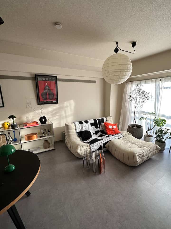 白とグレーのトーンの二人暮らしリビング、トーゴソファと植物が配置された明るく居心地の良い空間