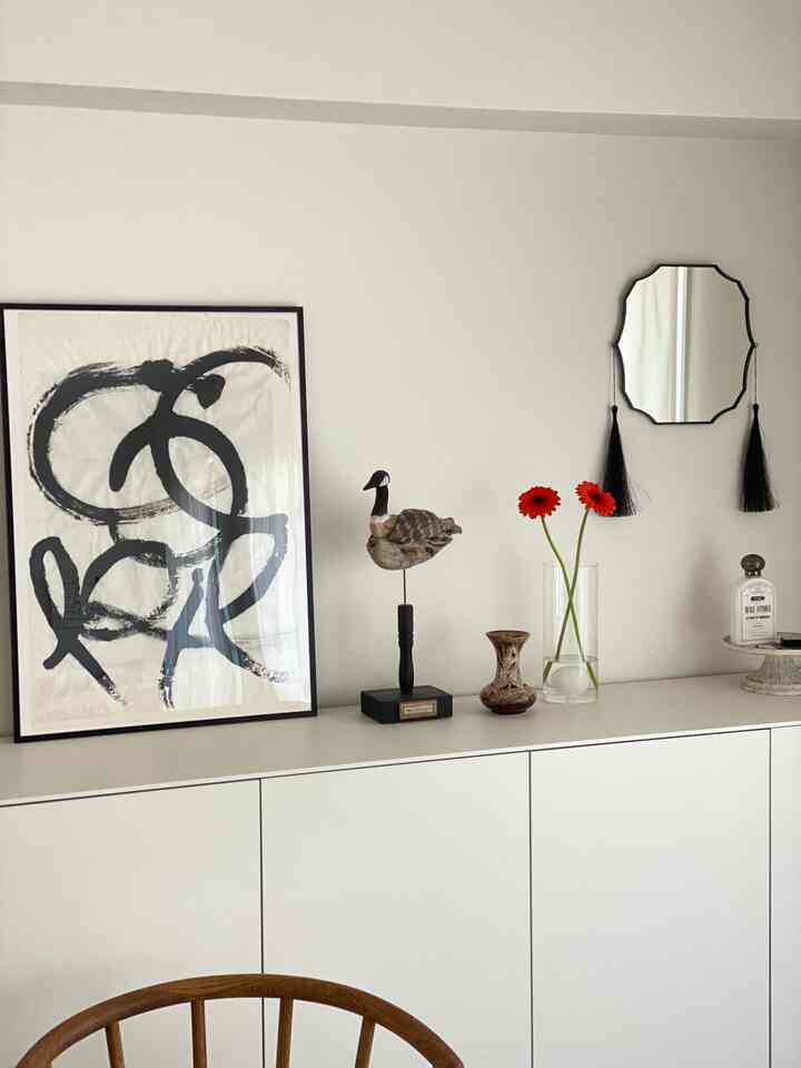 白を基調としたダイニングルーム、抽象的な書道アート、木製の椅子、花瓶、特徴的な鏡が配置されたモダンで落ち着いた雰囲気の空間
