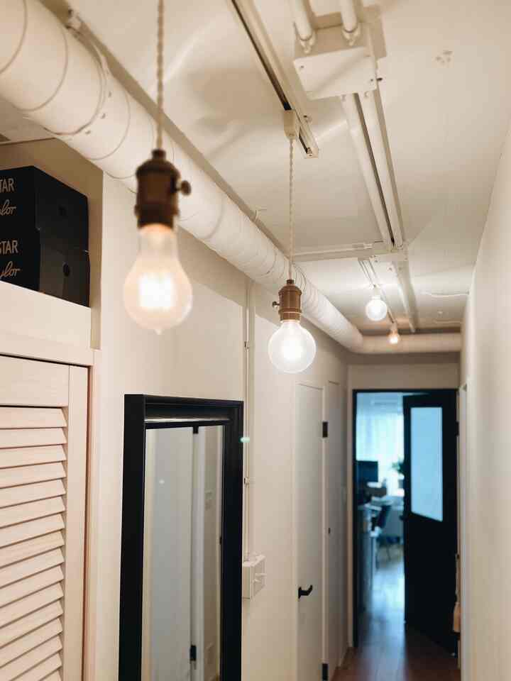 白を基調とした狭い玄関、エジソンバルブのペンダントライトと黒い鏡が配置された雰囲気のあるナチュラルな空間