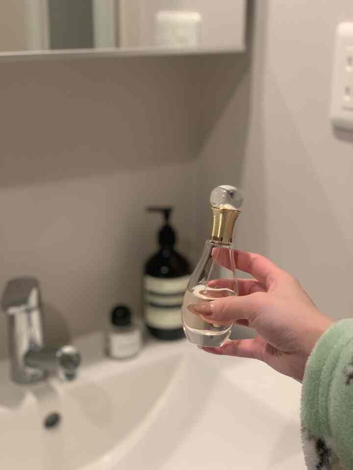 Monotone-toned powder room featuring a washbasin in center-left and a hand holding Dior perfume on right, simple and clean atmosphere