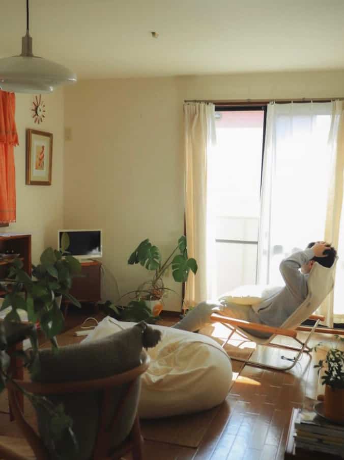 ナチュラルな色調のリビング、白いカーテンとソファ、木製のアームチェアが配置された雰囲気のある日差しの入る空間