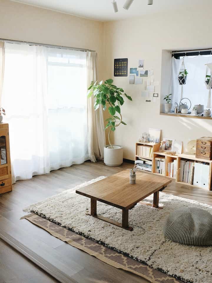 明るい白い壁とブラウンの木目調の1LDKリビング、木製テーブルとラグ、植物が配置された落ち着いたヴィンテージな空間