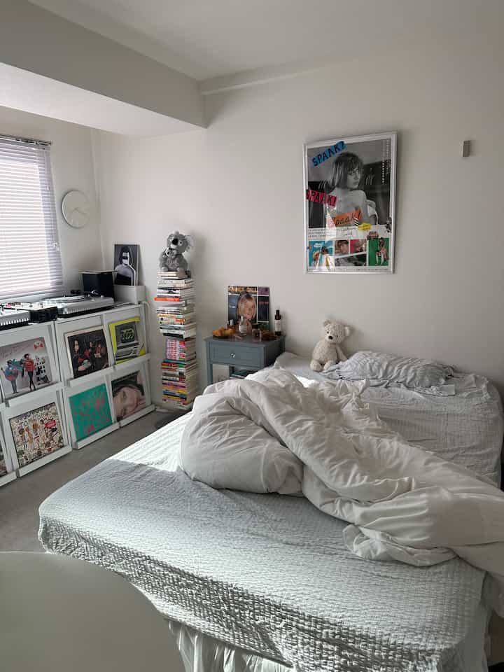 白と青の色調の寝室、本棚とポスターが配置されたミニマルな雰囲気のインテリア