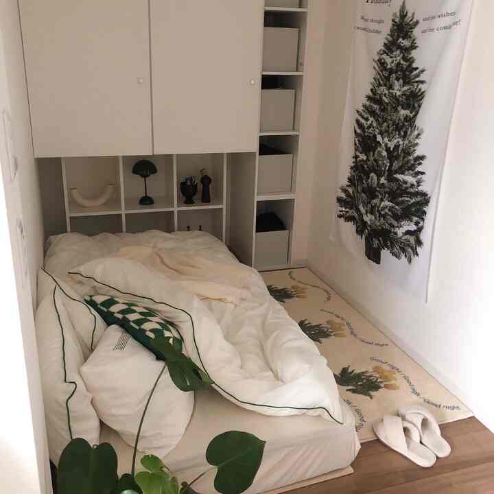 白と緑のトーンが特徴の狭く縦長の寝室、居心地の良いベッドと自然な植物要素が配置された雰囲気のあるインテリア