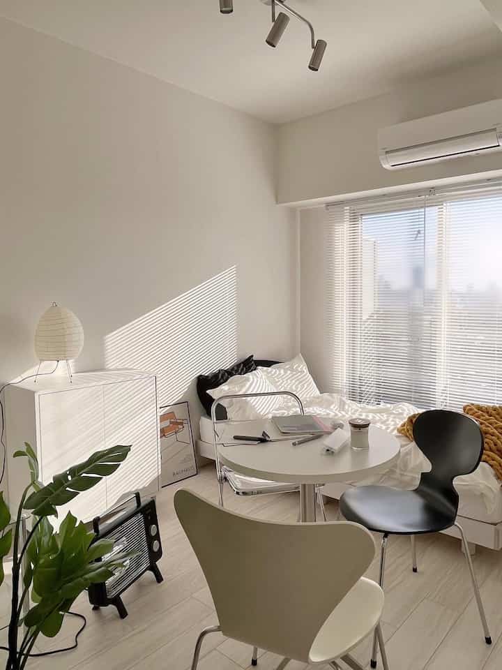 White minimal Nordic-style small bedroom featuring bed, round table with chairs, natural light and clean furniture arrangement