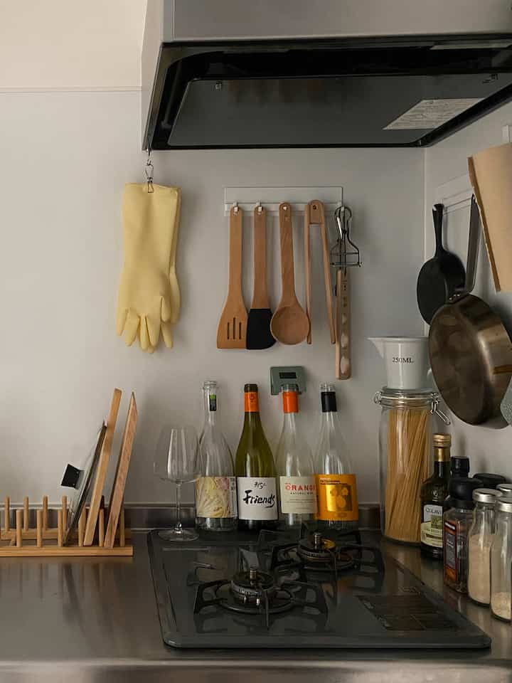 Kitchen with white walls and gray stove, featuring wooden kitchen utensils hanging on wall and wine bottles creating cozy home bar vibe