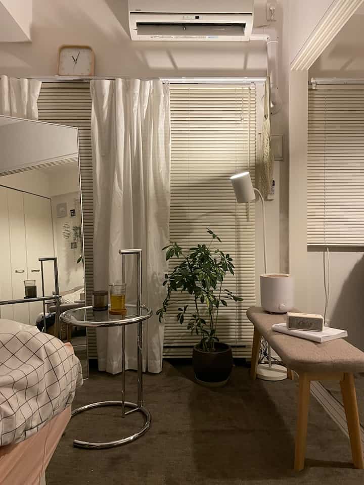 Calm brown carpet and white blinds in a small single household bedroom with wood-tone bench and round side table in natural style