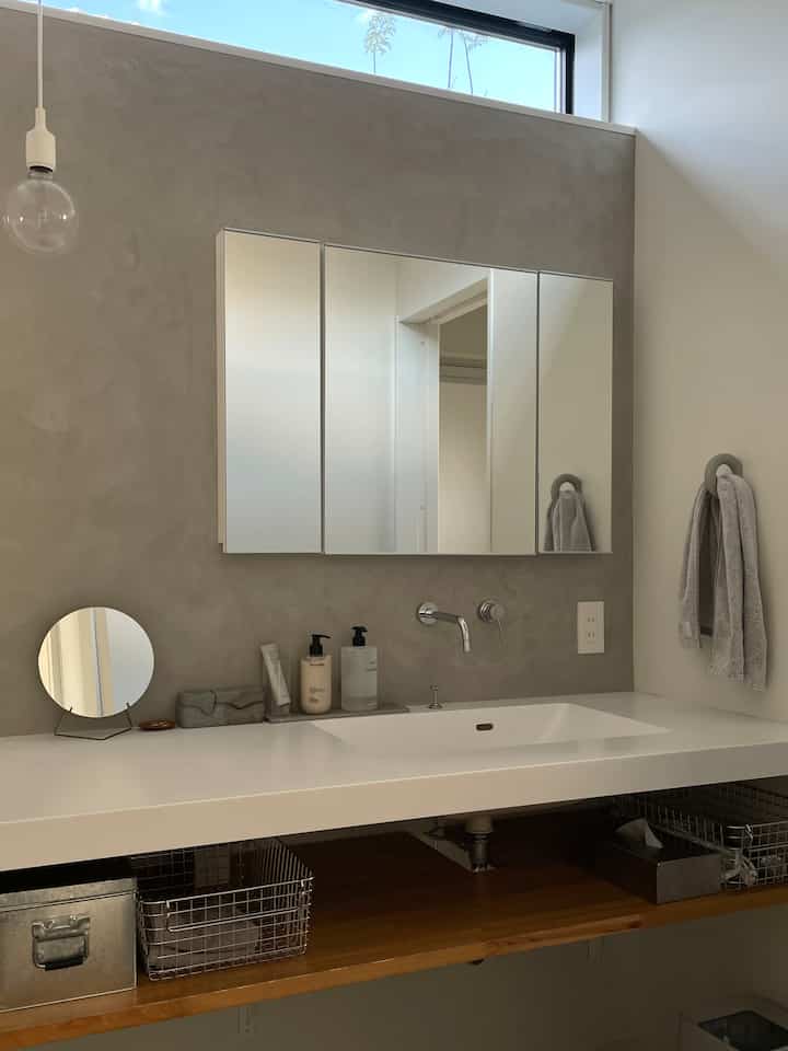 White and gray toned bathroom washbasin area featuring stainless steel storage baskets and a clean modern design