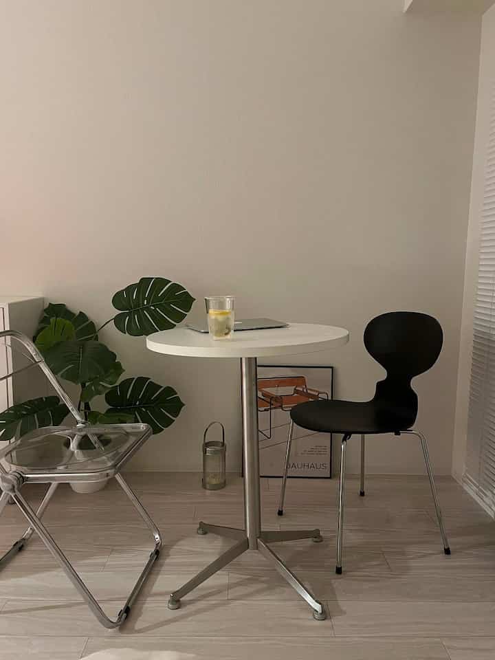 透明な椅子と黒いダイニングチェア、白い丸テーブル、モンステラのフェイクグリーンが配置された落ち着いたモダンなダイニング空間