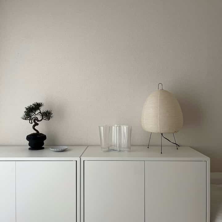 白を基調としたワンルーム空間、白い収納キャビネットの上に盆栽とあかりランプが配置されたシンプルでナチュラルなインテリア