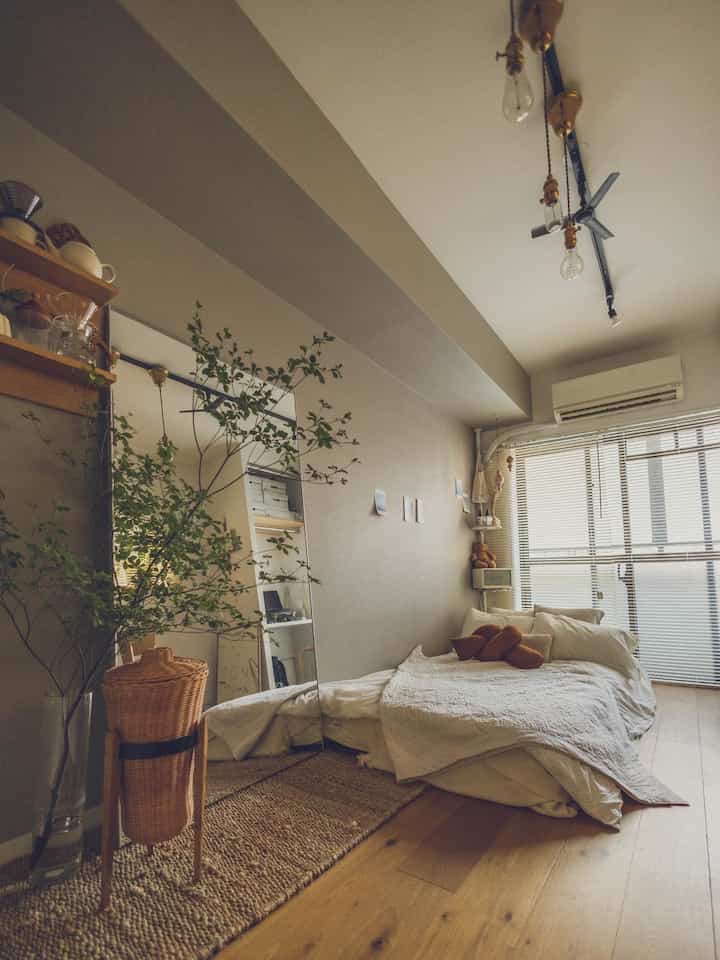 Warm natural-toned bedroom featuring wood tone flooring, large mirror, and plants creating a cozy atmosphere