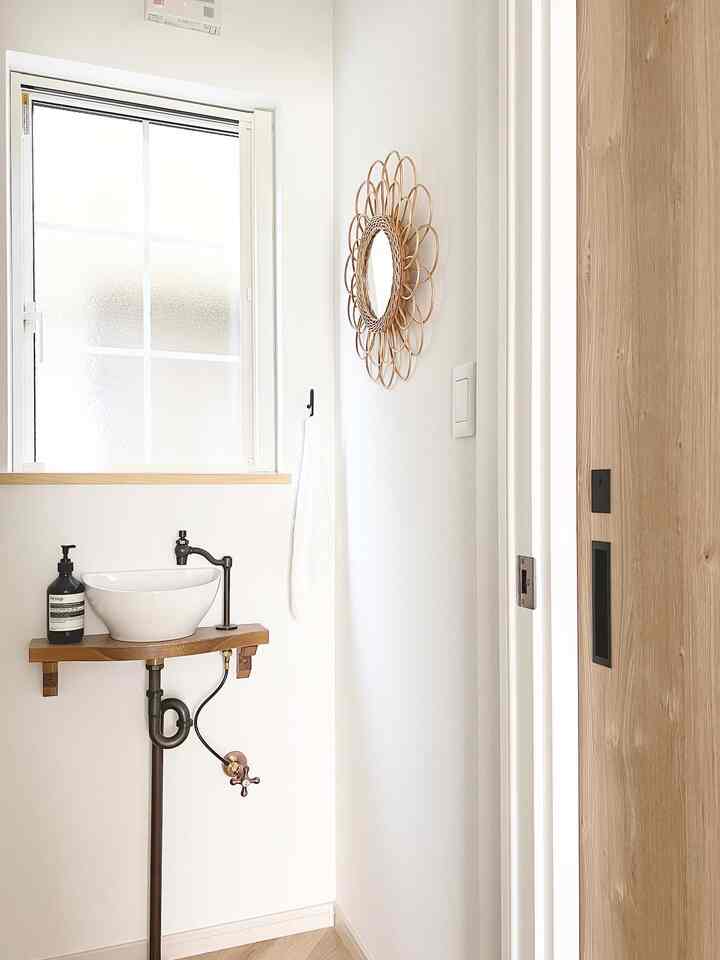 白と木目調のナチュラルなお手洗い、ラタンの鏡とコンパクトな洗面スペースが印象的な空間